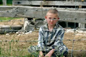 Pojken i randig pyjamas, Shmuel, sitter bakom taggtråd. Hans ansikte är smutsigt och hans blick är sorgsen.