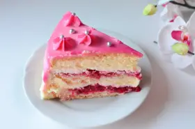 Pyszny tort malinowy z różowym lukrem i srebrnymi perełkami, przełożony kremem i malinową konfiturą.
