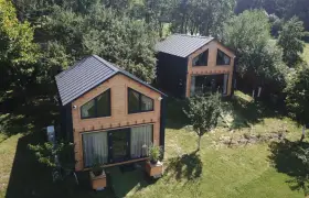 Dwa nowoczesne domki z drewna i czarnego panelu, idealne projekty domów pod wynajem, otoczone zielenią.