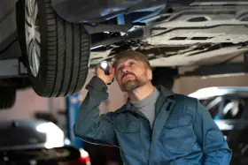 Mechanik z latarką bada podwozie auta, szukając problemów z jarzmem hamulca.