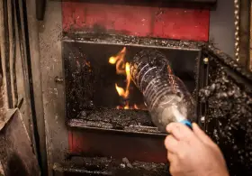 Ręka wrzuca plastikową butelkę do pieca. To może być mandat za palenie śmieci na podwórku.