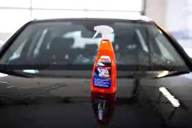 En flaska SONAX Xtreme Wet Coat står på en våt, mörk bilhuv.