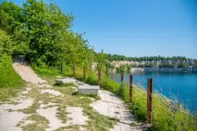 Ścieżka spacerowa nad turkusową wodą w kamieniołomie. Zakrzówek trasa zachęca do odpoczynku na ławkach wśród zieleni.