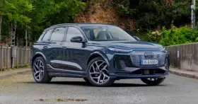 Elegancki, ciemnoniebieski Audi Q6 e-tron stoi na tle zieleni.