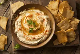 Houmous crémeux, garni de paprika et de persil, servi avec des chips pita croustillantes. Une recette houmous facile pour un apéritif gourmand.