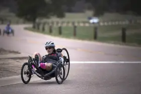 Kobieta w kasku i okularach przeciwsłonecznych na rowerze trójkołowym, intensywny trening HIIT na drodze.