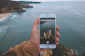 Dłoń trzyma iPhone'a 15, na ekranie widok klifów i oceanu. Czy iPhone 15 jest wodoszczelny? To pytanie zadaje sobie wielu podróżników.