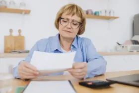 Zmartwiona kobieta w okularach analizuje dokumenty, zastanawiając się, ile lat pracy do emerytury jej pozostało.