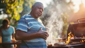 Mężczyzna z bólem w klatce piersiowej przy grillu. Może szuka czegoś, co neutralizuje kwas żołądkowy po obfitym posiłku.