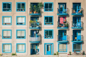 Elegancka loggia i balkon z niebieskimi ramami okiennymi, pełne zieleni i suszącego się prania, tworzą kolorowy kontrast na betonowej fasadzie.