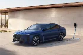 Elegancka, granatowa BMW hybryda podłączona do ładowarki przy nowoczesnym domu z widokiem na morze.
