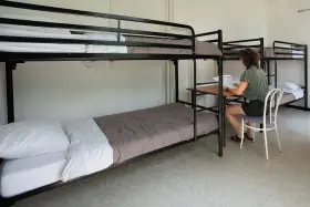 Chambre de l'auberge de jeunesse Camargue avec lits superposés. Une personne étudie à un bureau.