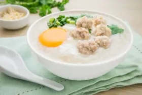 Miseczka pysznego congee z mięsnymi klopsikami, jajkiem i szczypiorkiem. Idealne na rozgrzewający posiłek.