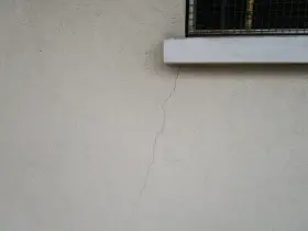 Crepa sottile su muro esterno, vicino a davanzale e inferriata. Necessaria riparazione crepe strutturali.
