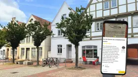 Blick auf die mittelalterliche Itzehoe Altstadt mit Fachwerkhäusern und einem Smartphone, das Informationen über die Stadt anzeigt.