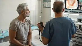 Lekarz wykonuje rektoskopię u pacjenta, obserwując obraz na monitorze.