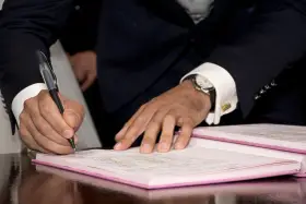 Mężczyzna w garniturze podpisuje dokument, co może oznaczać rozwiązanie umowy zlecenia za porozumieniem stron.