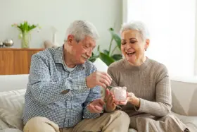 Szczęśliwa para seniorów wrzuca monety do świnki-skarbonki, planując spokojne przejście na emeryturę.