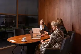 Trzy kobiety omawiają strategię w nowoczesnym biurze. Dyskretne spotkanie, które może dotyczyć usług private banking.