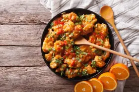 Sabroso pollo a la naranja, cubierto con salsa brillante y cebollín picado, servido con rodajas de naranja fresca.