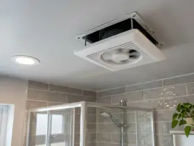 Extractor de baño siempre encendido, ventilando el espacio sobre la ducha. Una luz empotrada ilumina el techo.