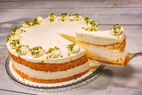 Eine Buttermilch Zitronen Torte mit cremiger Füllung und Pistazien-Deko. Ein Stück wird gerade herausgeschnitten.