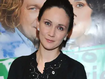 Ilona Ostrowska, znana z wielu filmów, pozuje z uśmiechem. W tle plakaty z innymi aktorami.