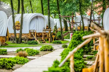 Wagony kempingowe w stylu western, idealne na weekend z Krakowa. Drewniane ścieżki i zielone krzewy tworzą malowniczy krajobraz.