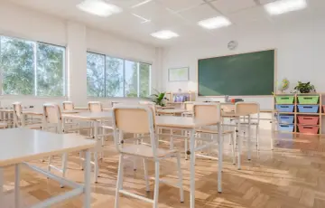 Puste ławki i krzesła w sali lekcyjnej, sugerujące rezygnację ze szkoły. Słońce wpada przez okna, oświetlając drewnianą podłogę.