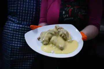 Porcja potrawki z kurczaka w kremowym sosie, podana na ryżu. Danie prezentowane na białym talerzu, trzymanym przez osobę w pomarańczowych rękawiczkach.