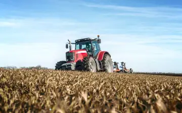Czerwony traktor orze pole. Rolnicy pracują, a pytanie czy rolnicy płacą podatek od nieruchomości pozostaje otwarte.