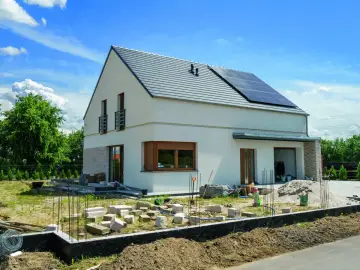 Nowy dom w budowie, z panelami słonecznymi na dachu. Wokół plac budowy, materiały i ziemia. To przykład nowoczesnej suchej zabudowy.