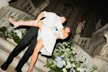 Un couple s'embrasse passionnément sur un escalier orné de fleurs, un moment clé pour réussir son mariage.