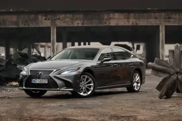 Szary Lexus LS 500h zaparkowany na tle zniszczonej budowli.