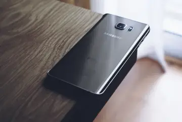 Czarny Samsung leży na drewnianym blacie. Chcesz wiedzieć, jak zresetować telefon Samsung?