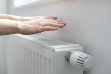 Dłonie ogrzewają się nad grzejnikiem, kiedy grzeją w blokach. Ciepło rozchodzi się po pokoju.