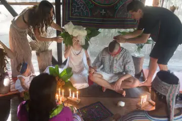 Ceremonia ślubna w Peru: para siedzi na podłodze, otoczona świecami i liśćmi, podczas gdy inni uczestnicy biorą udział.