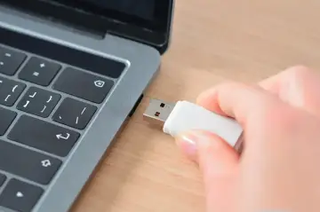 Dłoń wkłada pendrive do laptopa, przygotowując się do zapisania prezentacji Google na pendrive.