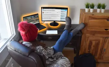 Osoba w czerwonej czapce i szarych kozakach uczy się, jak przenieść kursor na drugi monitor, korzystając z laptopa i zewnętrznego ekranu.