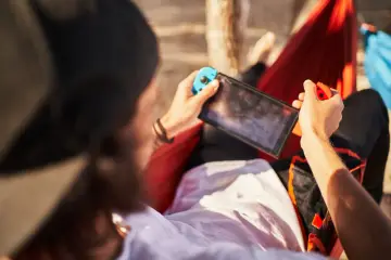 Osoba w hamaku gra na Nintendo Switch. Czas ładowania konsoli jest krótki, więc można grać wszędzie.