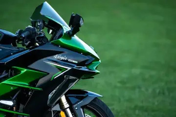 Błyszczący, czarno-zielony motocykl Kawasaki H2 SX z napisem "Ninja H2 SX" na owiewce, zaparkowany na tle zielonej trawy.