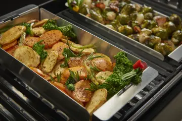 Pyszne warzywa, takie jak marchewka i ziemniaki, pieczone w metalowym koszu do grilowania, z dodatkiem ziół i jarmużu.