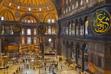 Wnętrze Hagia Sophia z ogromnymi okrągłymi kaligrafiami i turystami.