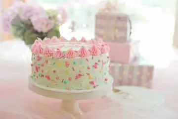 Jasnozielony tort z różową posypką i kremem, obok prezenty. Zastanawiasz się, ile kosztują torty na przyjęcie?