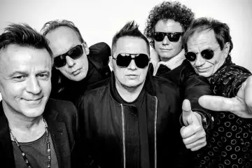 Pięciu mężczyzn w okularach przeciwsłonecznych, gotowych na koncert. Jeden z nich pokazuje kciuk w górę, jakby mówił "t.love hau! hau!".