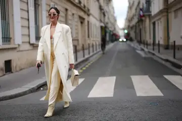 Elegancka kobieta w kremowym płaszczu i spodniach, spacerująca po paryskiej ulicy, uosabia szyk francuskich marek modowych.