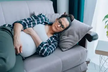 Kobieta w ciąży leży na kanapie, cierpiąc z powodu objawów listeriozy.