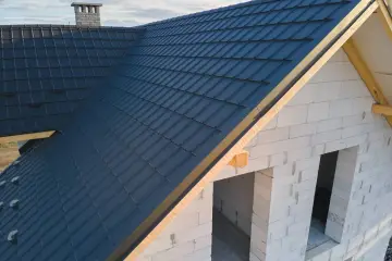 Nowy dach z ciemnogranatowej blachodachówki, wiatrownica zamontowana. Trwa obróbka dachu.