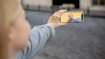 Kobieta trzyma telefon, by nagrać ekran z uśmiechniętą twarzą na żółtym tle.