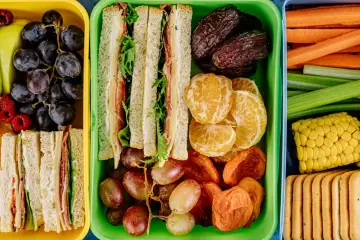 Kolorowe pojemniki pełne niskokaloryczne przekąski: kanapki, owoce, warzywa i ciastka. Idealne na zdrowy lunch.